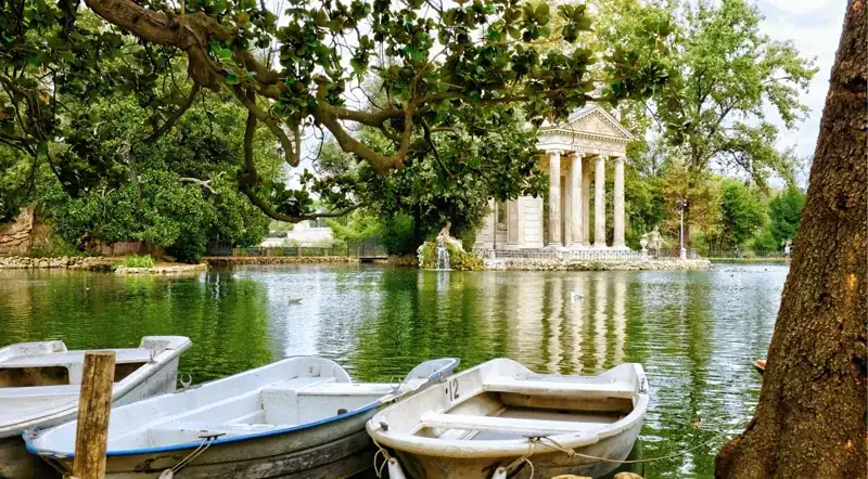 Rowboats on the Villa Borghese park lake framed by trees, near the gallery entrance